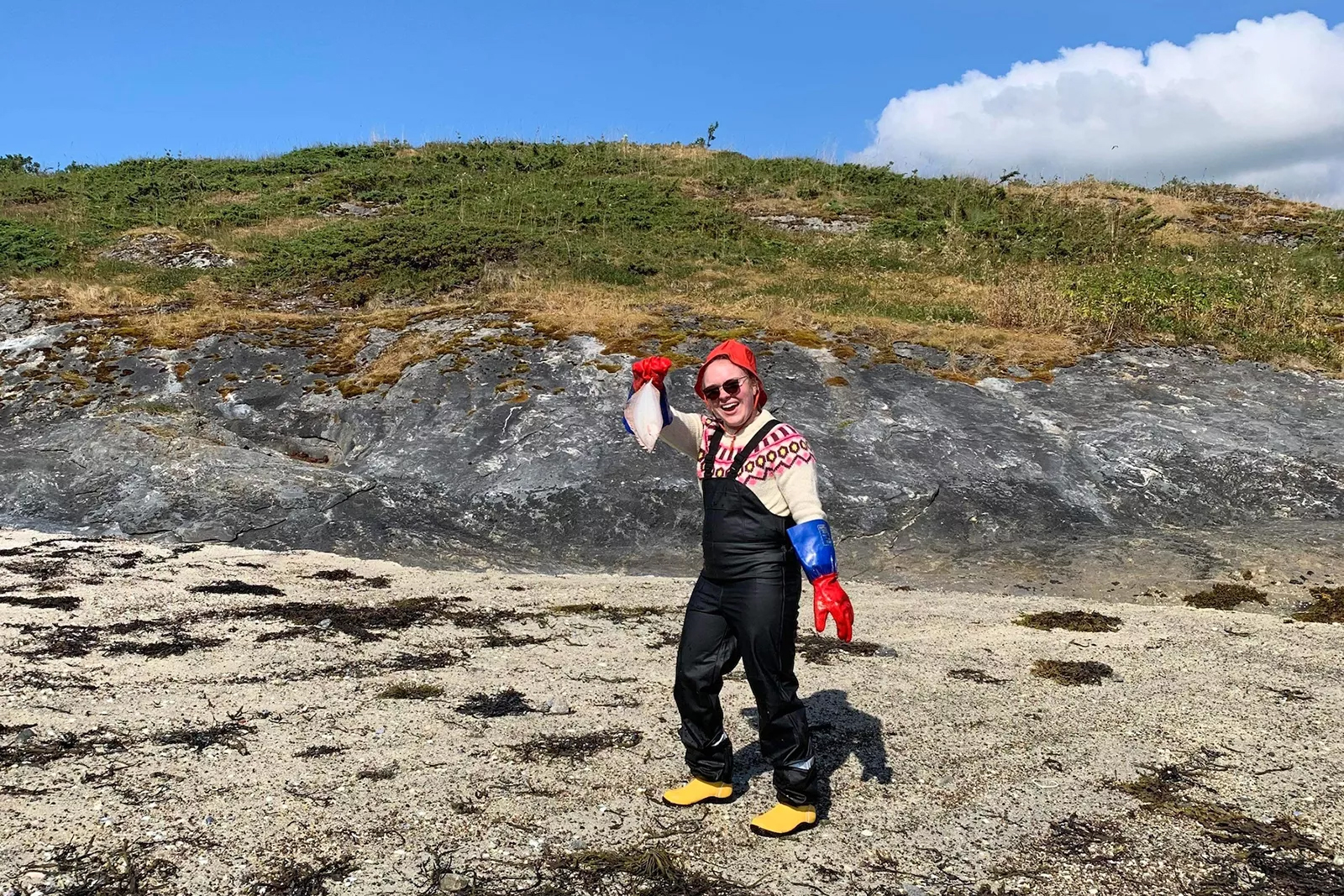 Andrea Haukebøe Micheeff står på en strand og holder opp en fisk mens hun smiler