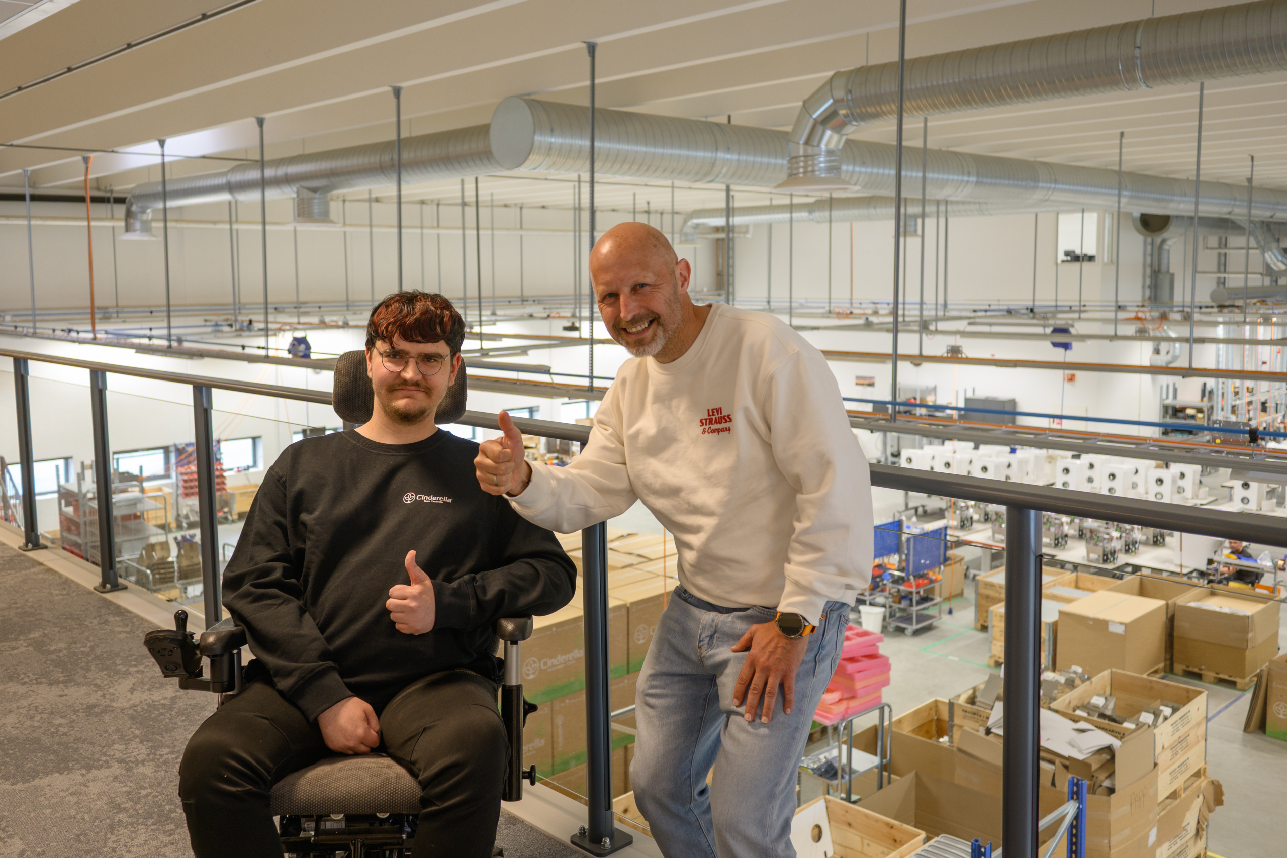 Ny fagarbeider i IT-drift poserer sammen med fagansvarlig - i bakgrunnen kan man se innvendig fabrikken hvor produksjonsbedriften holder til